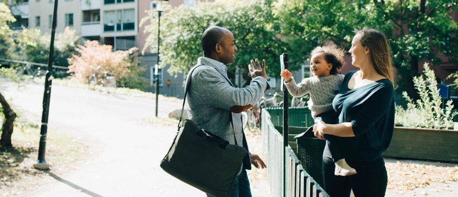 Un père salue son enfant, dans les bras de sa mère, en partant au travail